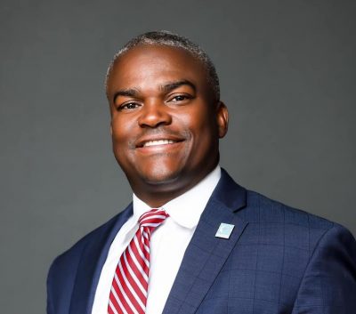 A man in a suit and tie, smiling warmly, showcasing a professional and approachable demeanor.